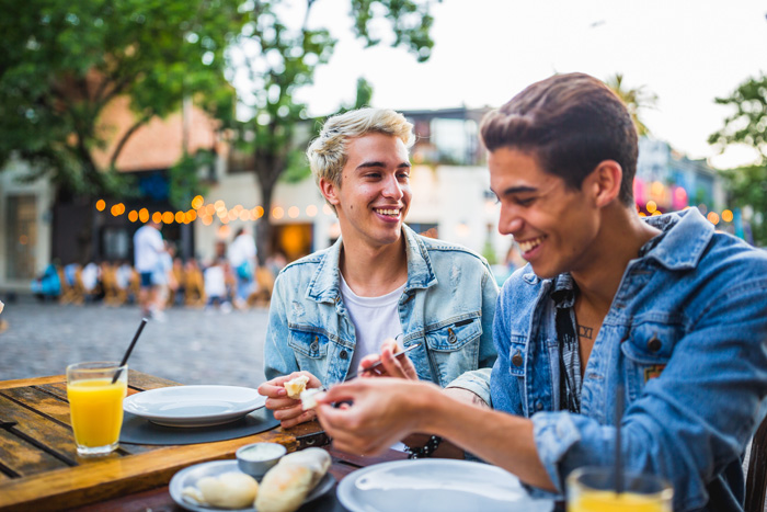 two young people smiling and enjoying food at an outdoor table